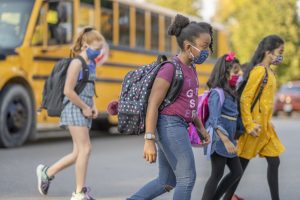 Students crossing the street wearing masks after getting off the school bus.