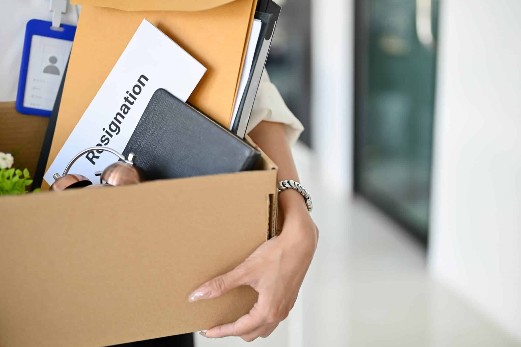 Close-up image of a female office worker holding a box with her belongings and a resignation letter