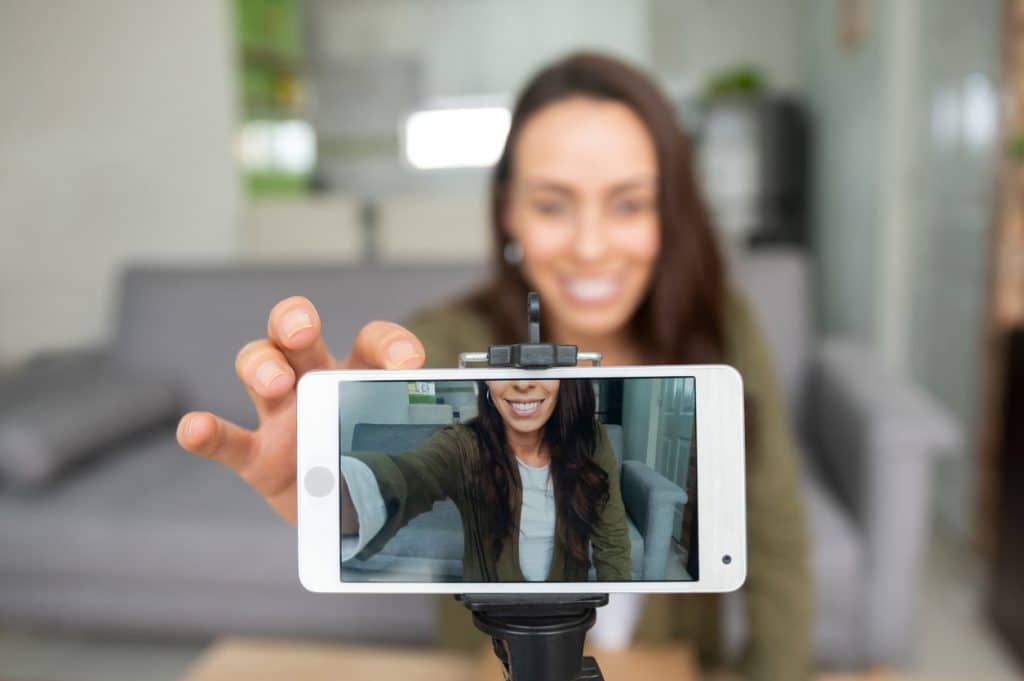 Happy female vlogger recording content at home using her cell phone while staying at home - lifestyle concepts