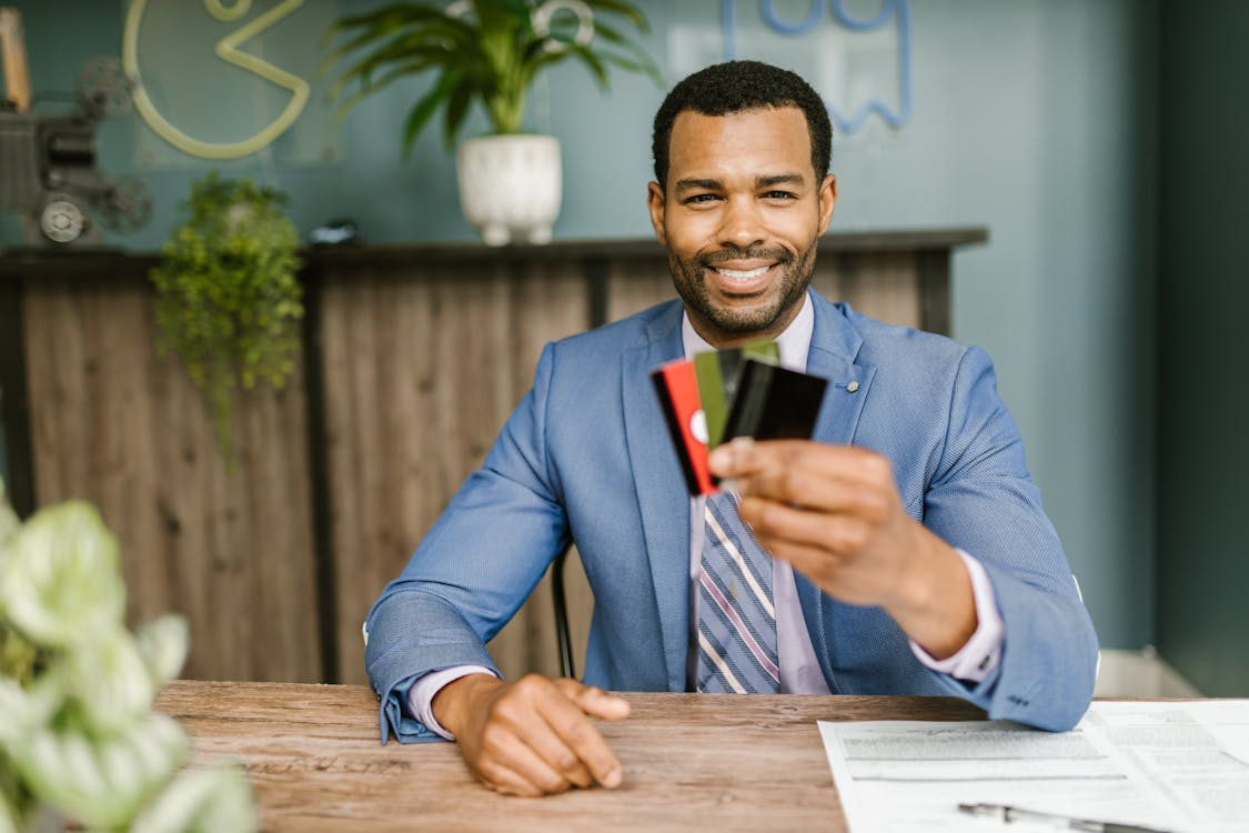 Image of a man holding up three credit cards, elbows resting on a table with papers.